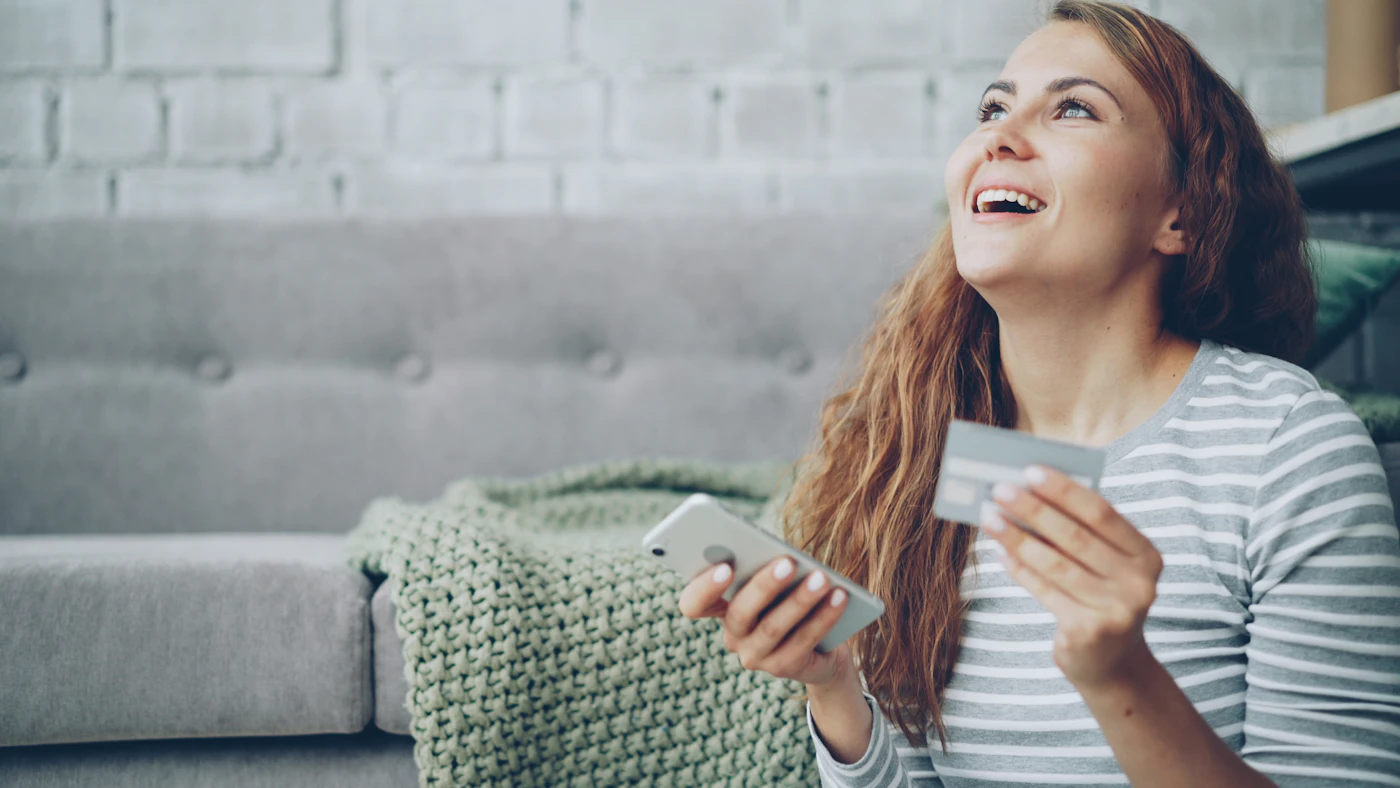 Joueuse souriante tenant une carte de crédit et un téléphone pour un dépôt en ligne
